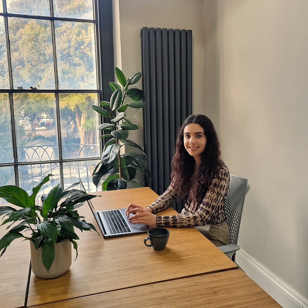 A smiling woman sat at a desk in one of the serviced offices at The Workplace, furnished with bamboo desks and comfortable chairs.