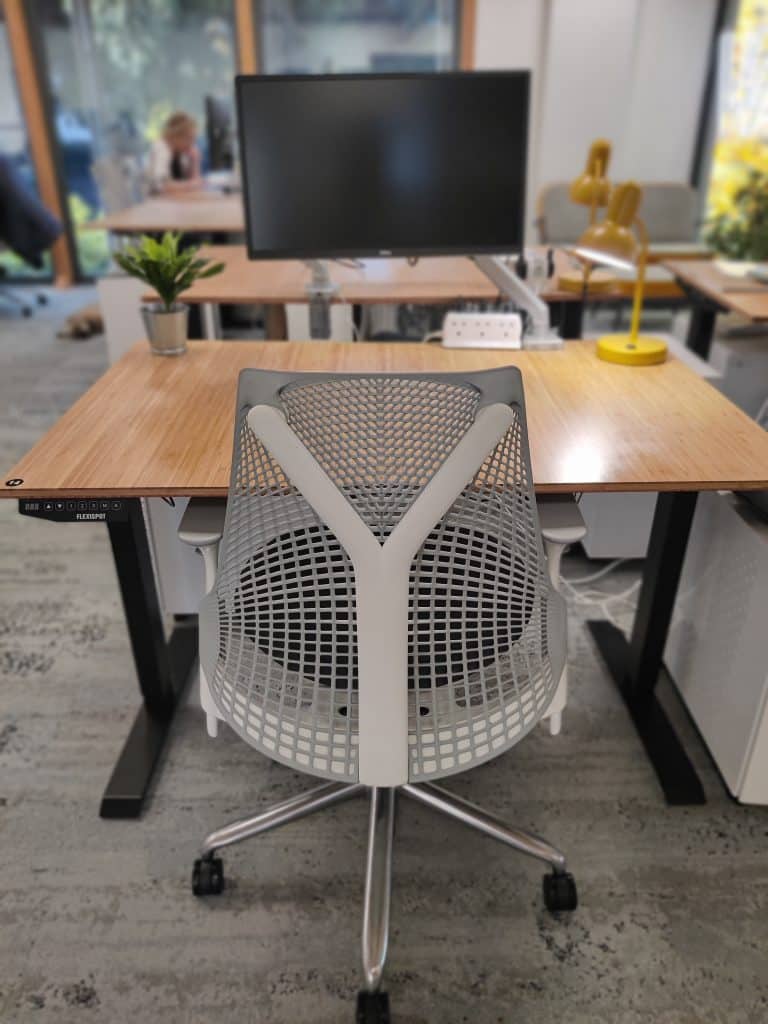 A coworking desk with a Herman Miller chair, bamboo desk, and a montior screen
