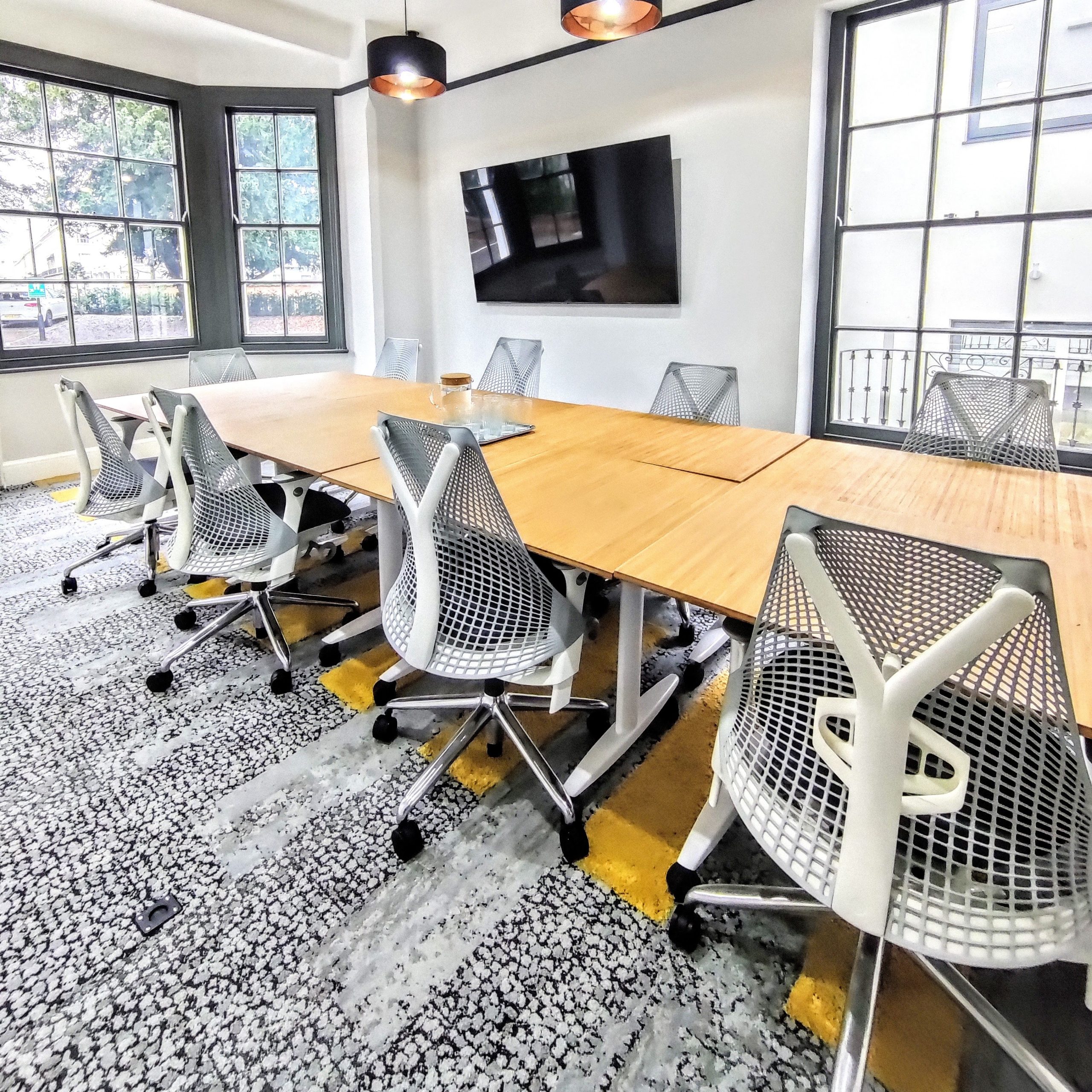 A light-filled, spacious meeting room with a monitor, large windows, and comfortable seating.