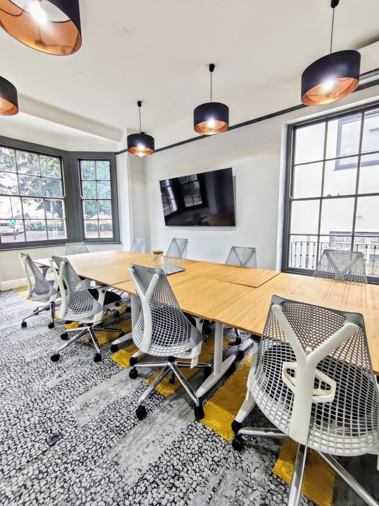 A large meeting room with a monitor, boardroom-style setup, and Herman Miller chairs.