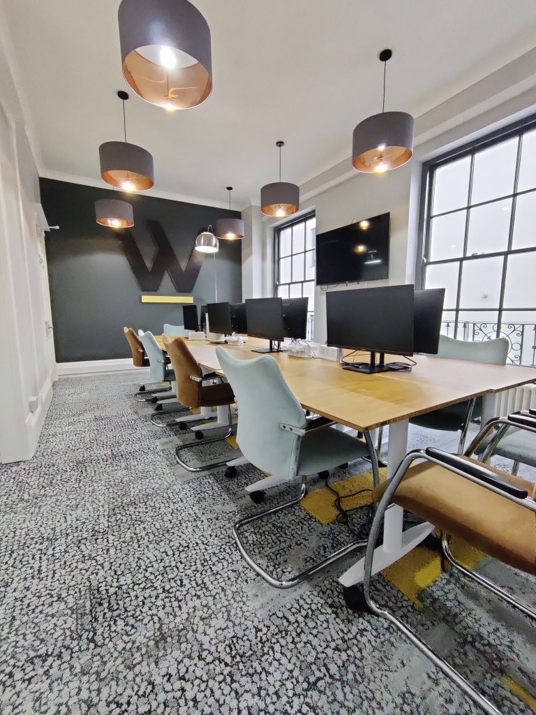 A large meeting room with a boardroom-style setup and monitors with a large screen on the wall.