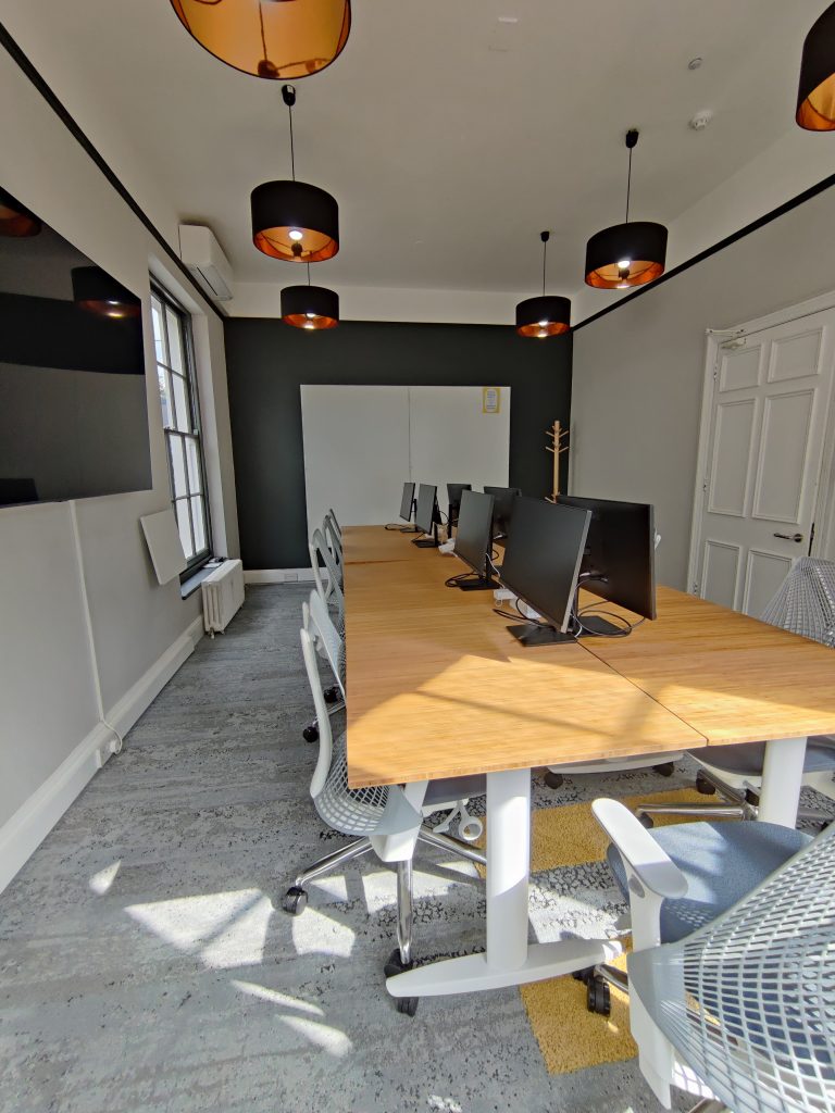 A large meeting room with Herman Miller chairs, screen, whiteboard, and monitors.
