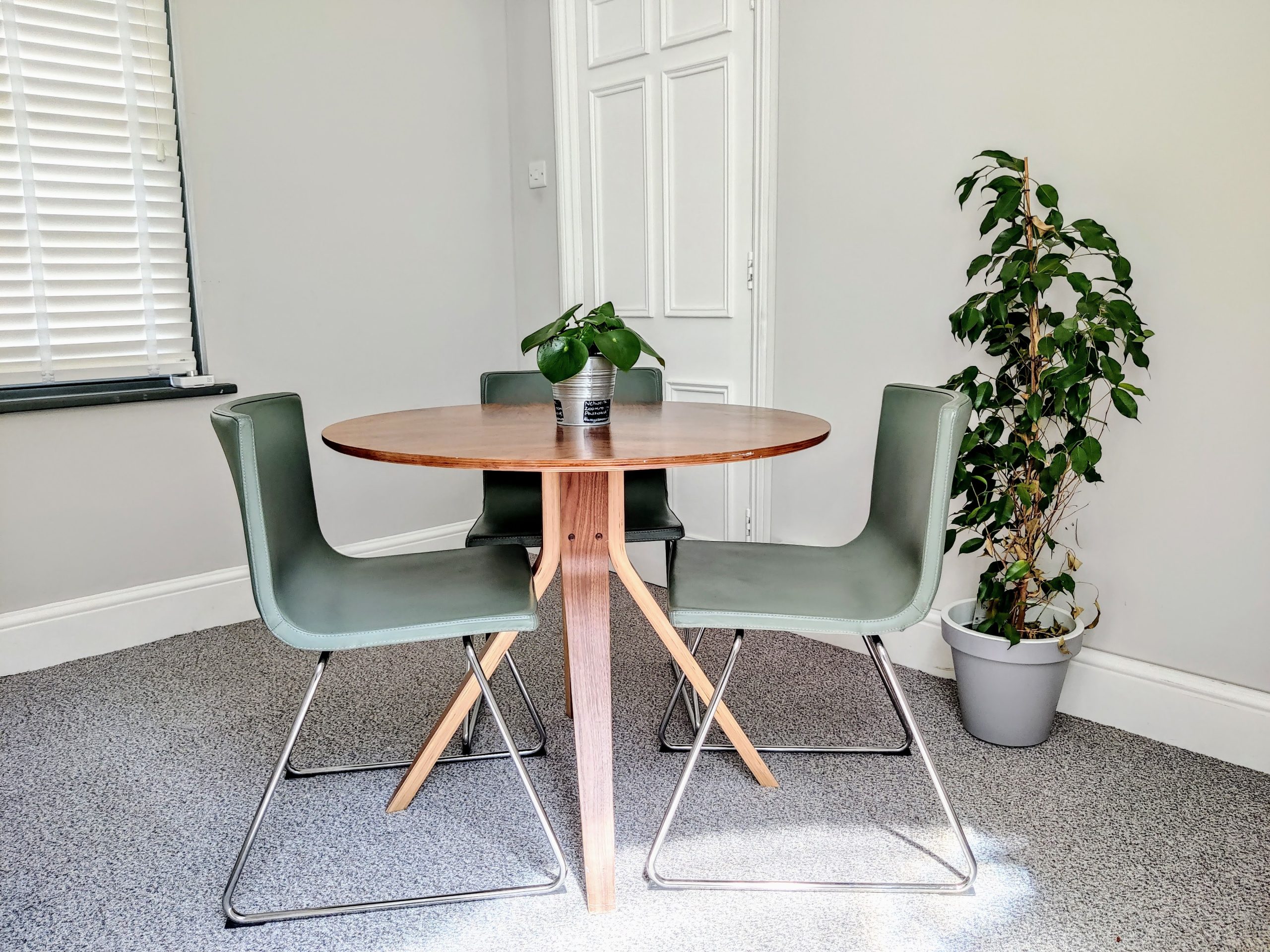 A small meeting room with 3 chairs around a circular table and plants in the background.