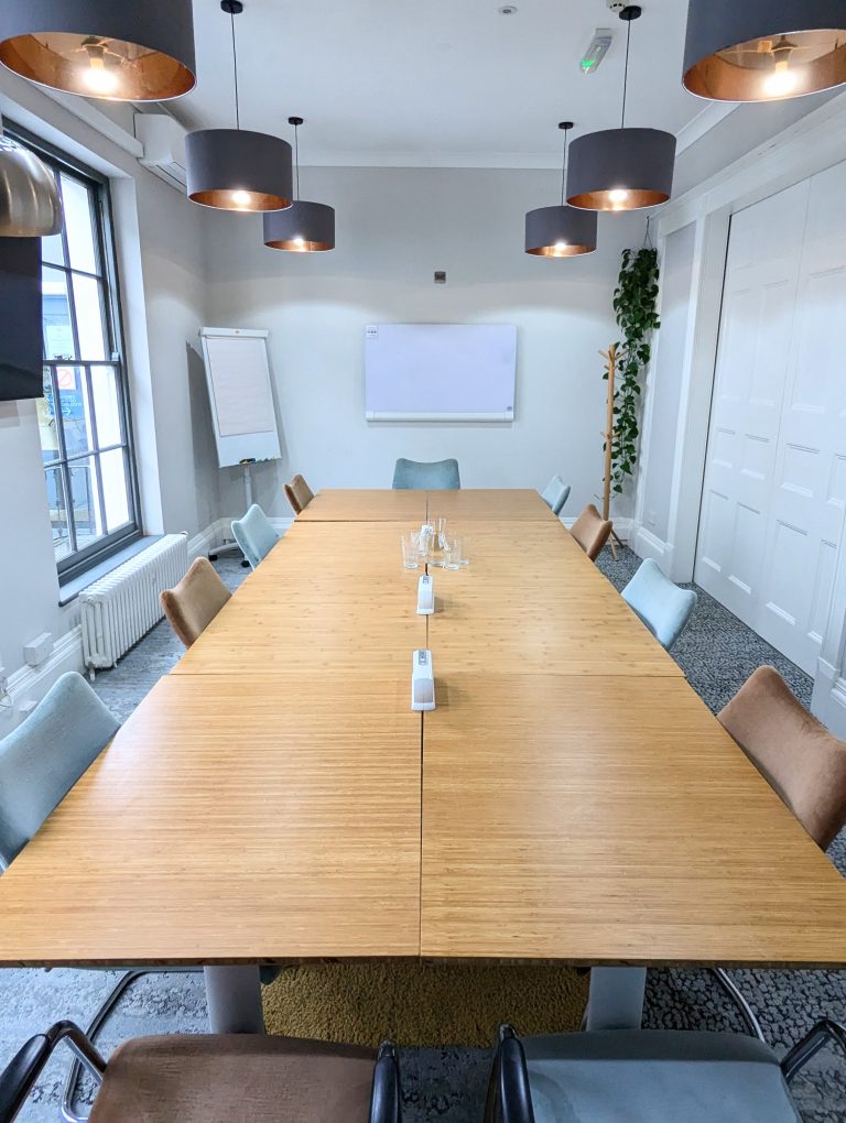 A large meeting room with a boardroom-style setup, whiteboard, flipchart, and large chairs.