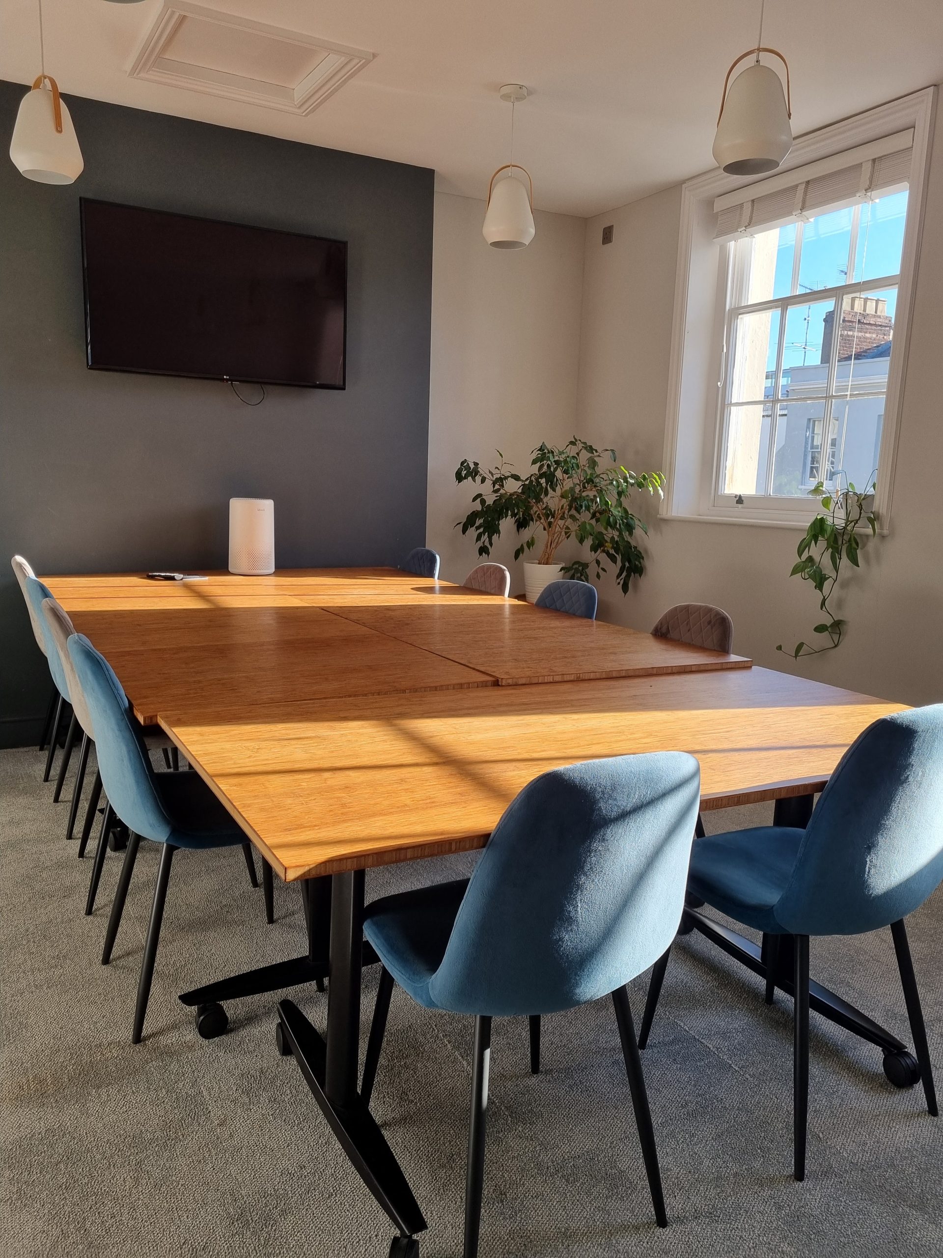 A bright, sunny meeting room with 10 seats, large screen, and bamboo desks.