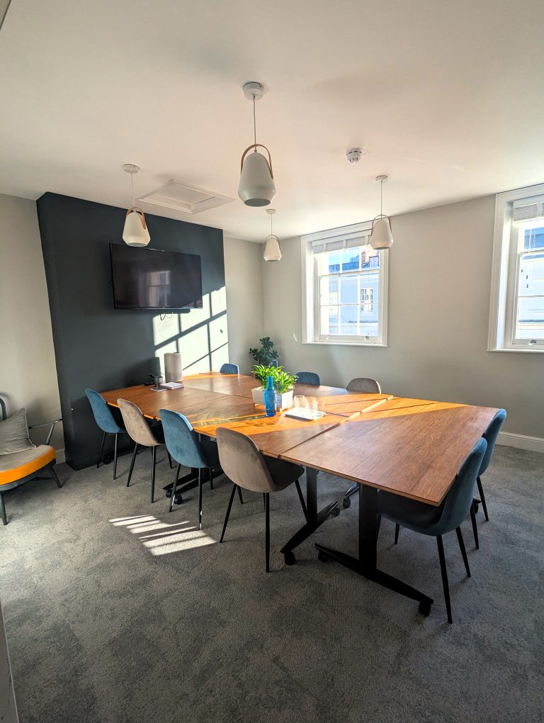 A sunny meeting room with 10 chairs, a large screen, and big windows.