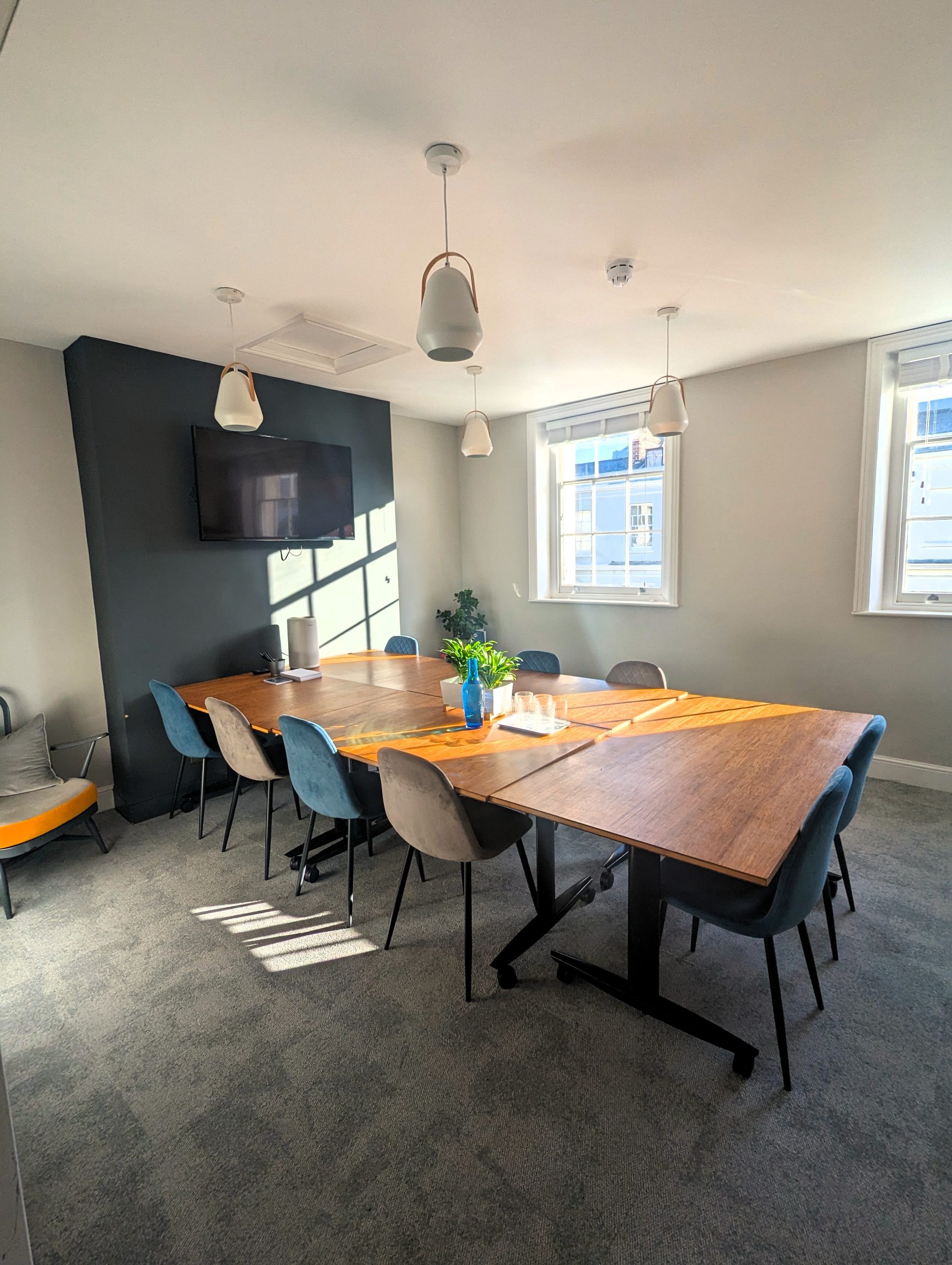 A sunny meeting room with 10 chairs, a large screen, and big windows.